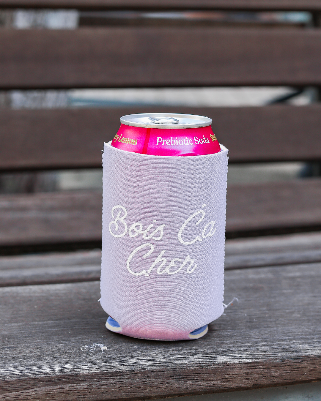 Can with a soft lavender label on a white can cooler with 'Bois Ca Cher' text, placed on a wooden surface.
