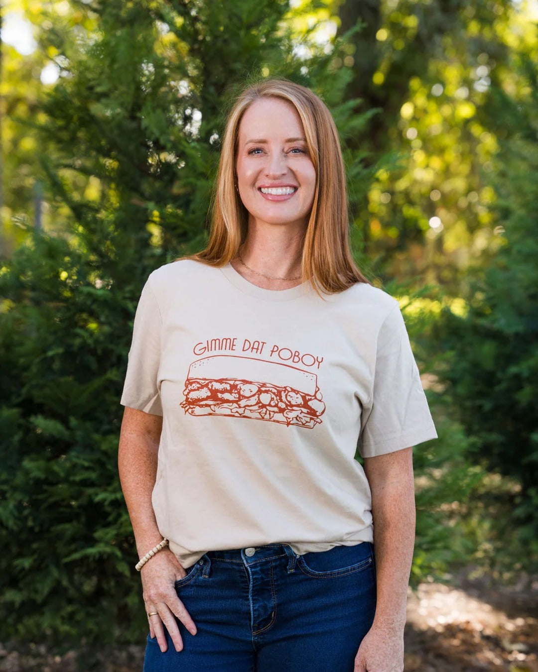 Woman wearing the Gimme Dat Poboy T-Shirt in tan with jeans, a Louisiana po'boy tee by Sweet Baton Rouge