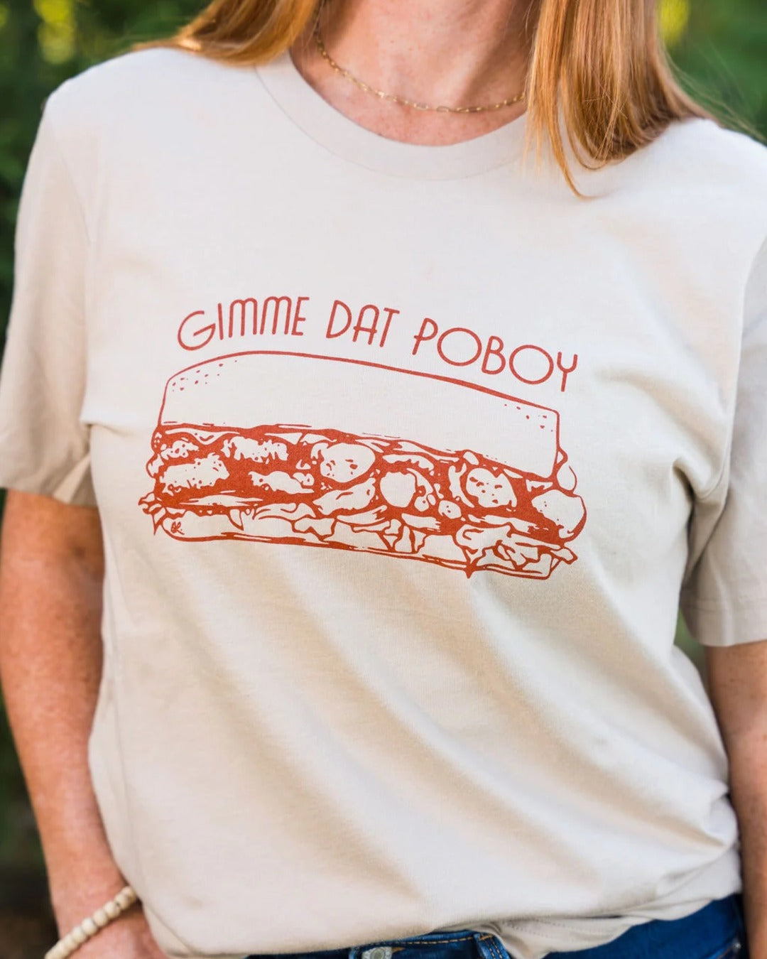Close-up of the rust orange Gimme Dat Poboy sandwich screen print on the tan t-shirt