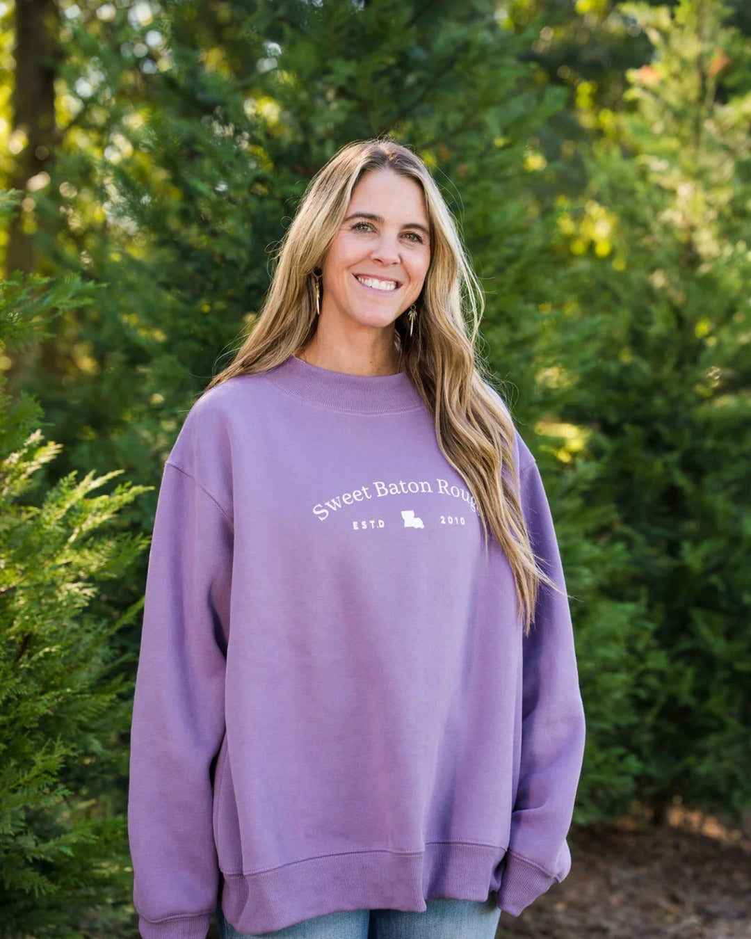 Smiling model in the lavender Sweet Baton Rouge Travels oversized mock neck sweatshirt outdoors