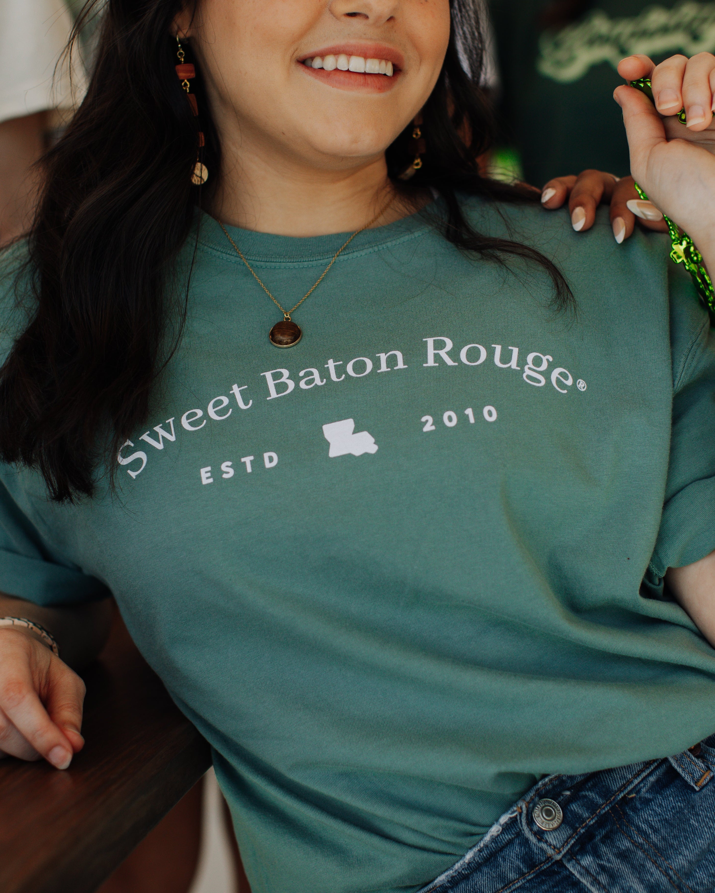 Person wearing a light green t-shirt with 'Sweet Baton Rouge' text, holding green beads for St Patricks Day, Wearin' of the green parade.